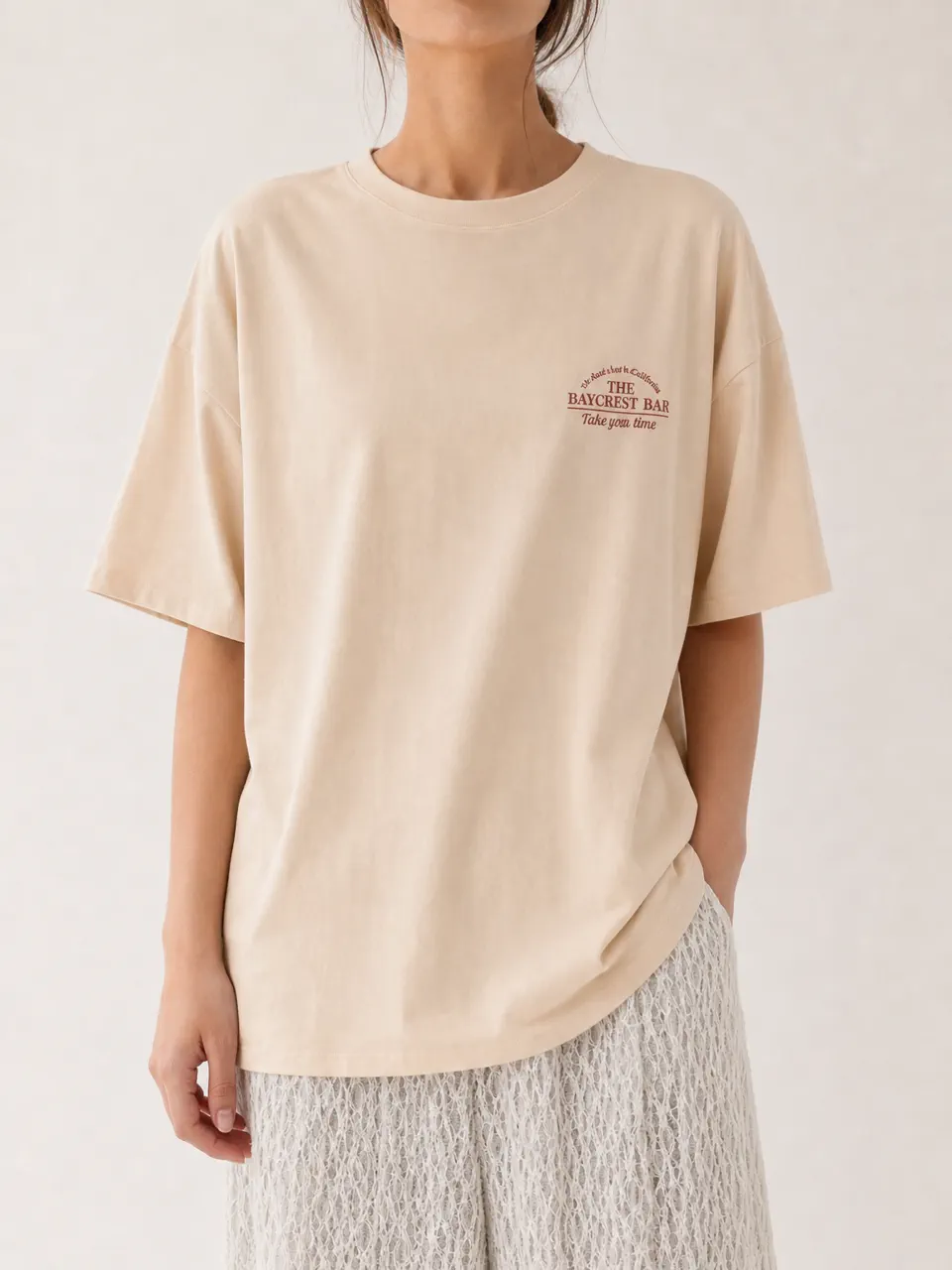 胸元にワンポイントロゴを配したクリーム色のオーバーサイズTシャツ