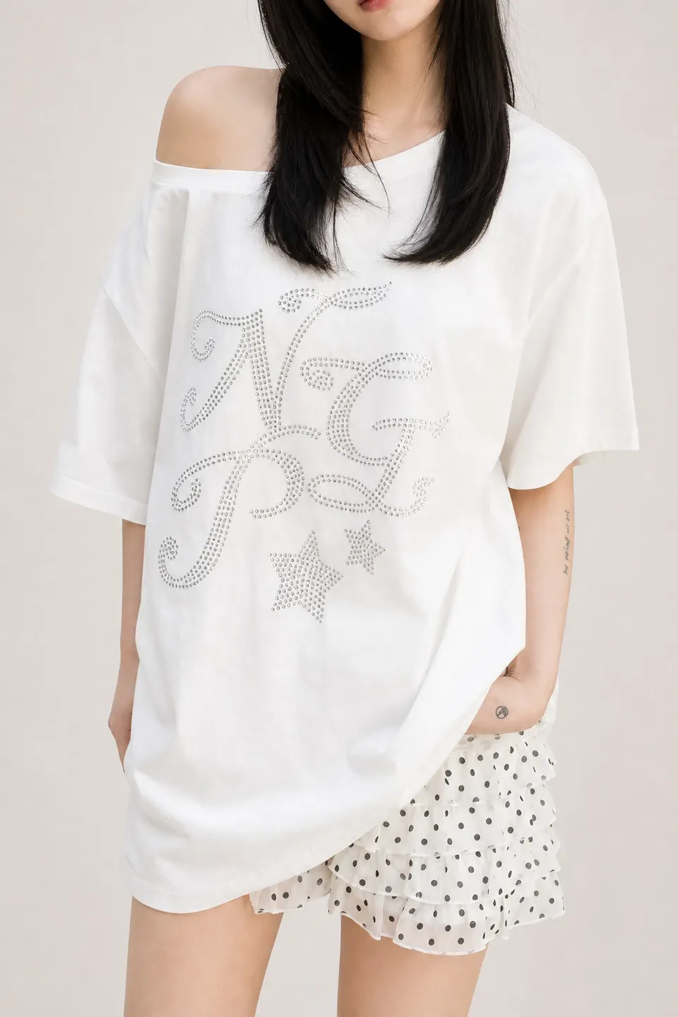 ラインストーンのグラフィックを施した白のオーバーサイズ・オフショルダーY2K Tシャツ。甘辛系レディース商品の開発参考