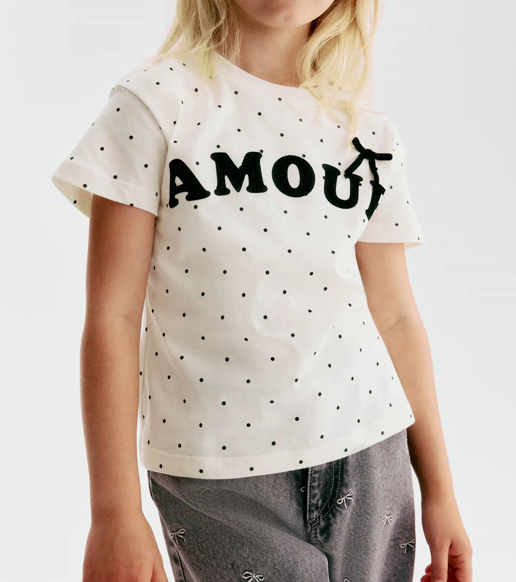 Weißes Kinder-T-Shirt mit schwarzen Punkten, AMOUR-Logo und Schleife